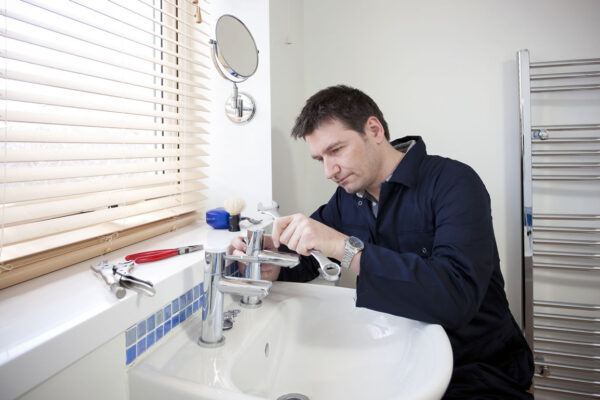 Man repairing a bathroom sink faucet with tools