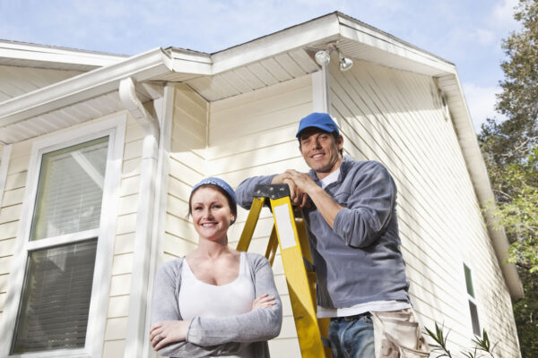 Smiling couple standing by a ladder in front of a renovated house
