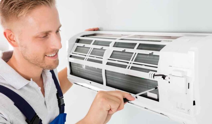 A technician performing AC repair Dubai on a wall-mounted split air conditioner, removing the front panel to inspect and clean internal components.
