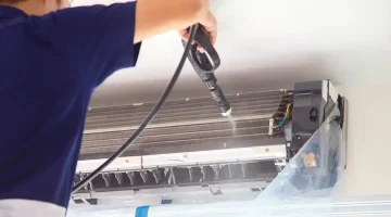 Worker using high-pressure spray to clean AC coils.