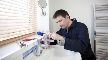 Man repairing a bathroom sink faucet with tools