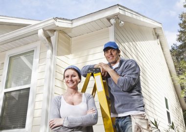 project02 Smiling couple standing by a ladder in front of a renovated house