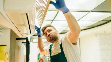 Technician lifting an AC filter cover to clean air ducts.